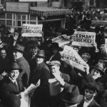 A crowd in Times Square hold up copies of newspapers with a headline about the signing of the Armistice